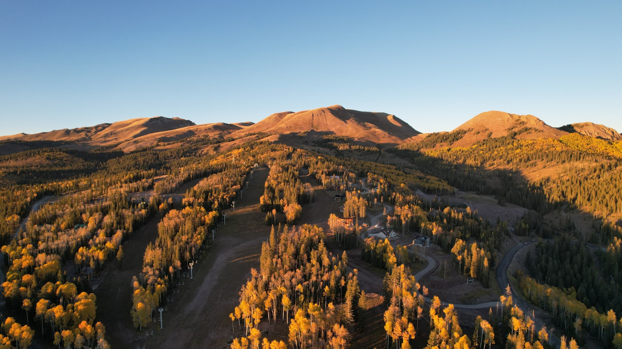 Aerial view of golden aspen forests and mountain ridgelines at sunrise