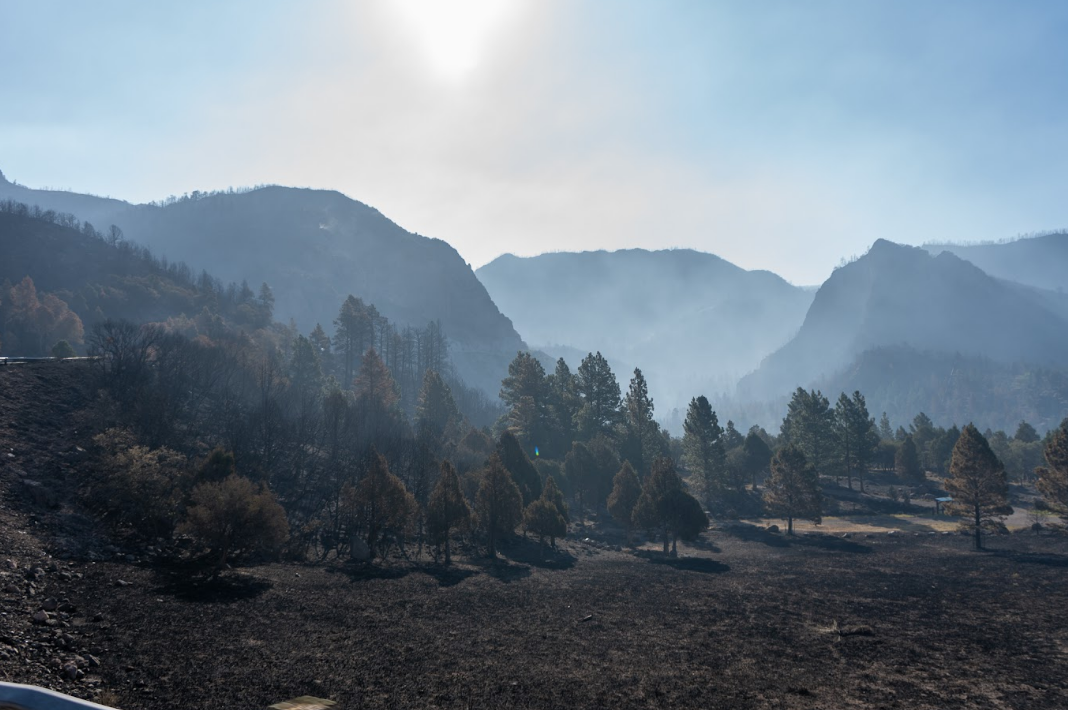Smoke-filled mountain valley with charred ground and hazy ridgelines after the Cottonwood Fire